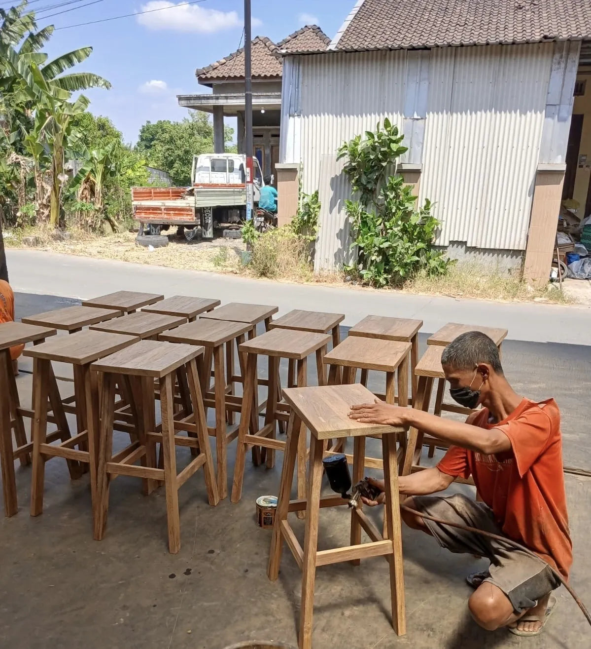 Indonesische medewerker van Tall Men Standing die met de hand bezig is met een teakhouten kruk
