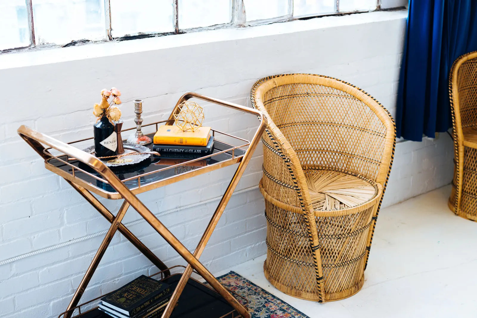 Rotan stoel naast een bijzettafel met boeken en een vaas in een licht, rustig interieur