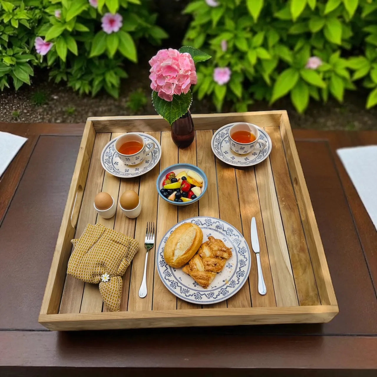 Klein dienblad van teakhout in naturel kleur met daarop eten, drinken, bestek en bloemen