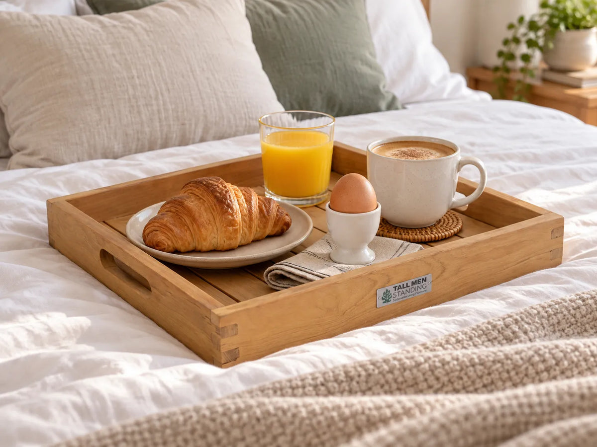 Teakhouten dienblad met handgrepen op een opgemaakt bed, met een croissant, sinaasappelsap, een gekookt eitje en een kop koffie voor ontbijt op bed