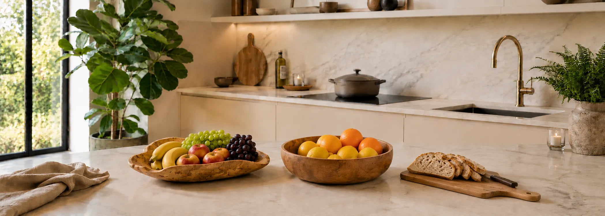Teakhouten schalen en snijplank in een keuken. Schalen zijn gevuld met fruit zoals; appels, bananen, druiven, citroenen en sinaasappels en op de snijplank ligt brood