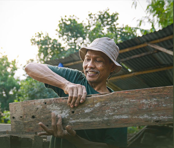 Indonesische man die teakhout aan het tillen is met zijn handen en glimlacht