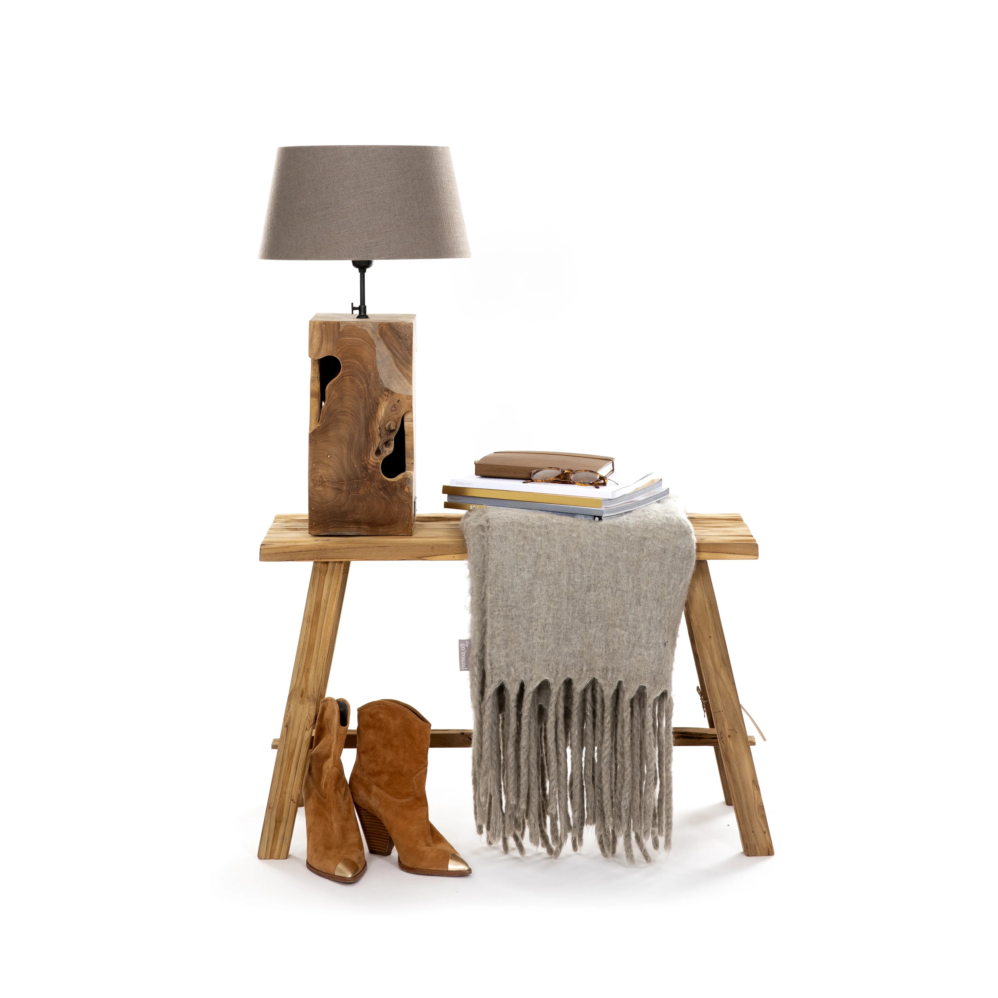 Vintage teakhouten bank gebruikt als bijzettafel met verschillende producten zoals houten lamp, deken, boeken en laarzen